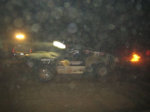 1990 Ford Bronco - off-road race truck numbered 27 with BFGoodrich and beadlock decals kicks up dust racing past a small fire at night.