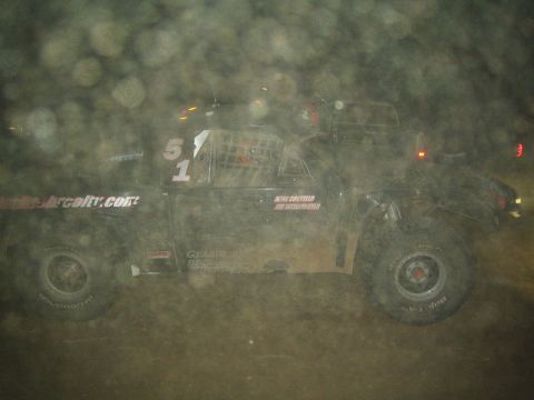 1990 Ford Bronco - black off-road race truck numbered 51 with website and BFGoodrich decals races over dirt at night through a hazy foreground.