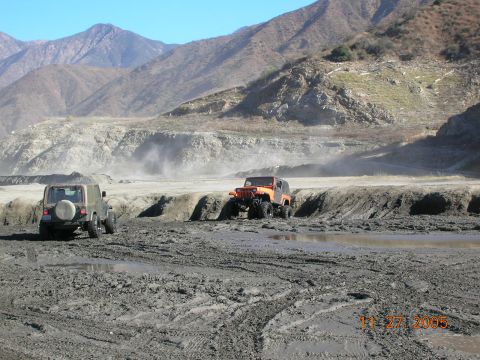 1985 Ford Bronco - Two off-road vehicles navigate a muddy terrain with a mountainous backdrop, captured on November 27, 2005.