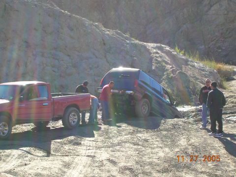 1985 Ford Bronco - Two vehicles are in a muddy, off-road environment with people around them.