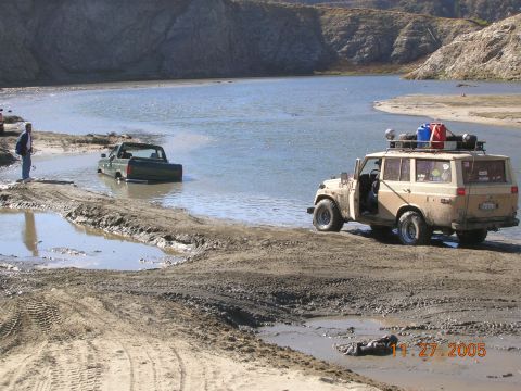 1985 Ford Bronco - Two off-road vehicles navigate through a body of water on a sunny day.
