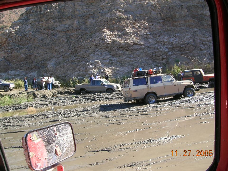Tan SUV with luggage on roof stuck in mud, viewed from inside another vehicle