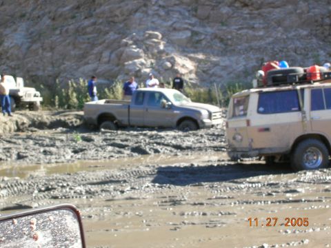 1985 Ford Bronco - Several vehicles are stuck in a muddy off-road area, with people observing the situation.