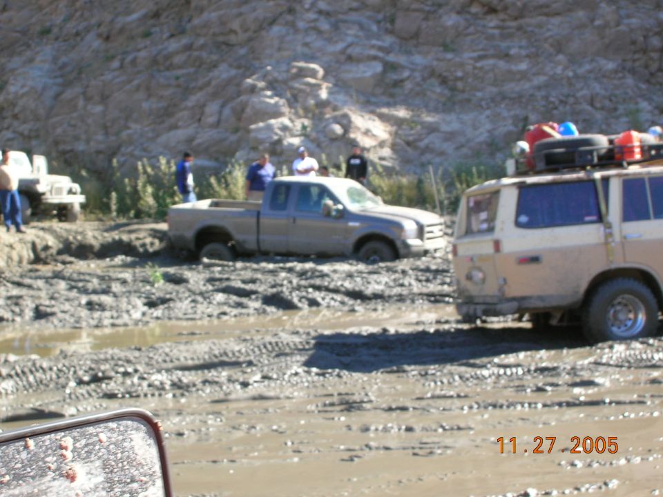 Pickup truck stuck in mud with a van and another vehicle nearby. People are standing around