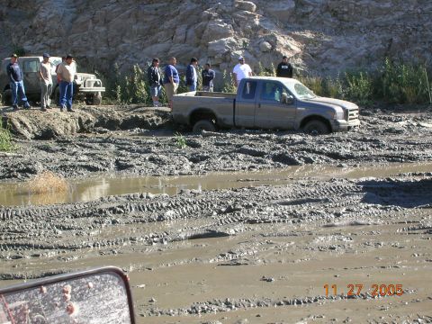 1985 Ford Bronco - Multiple vehicles and people are present near a Ford F-Series truck stuck in thick mud.