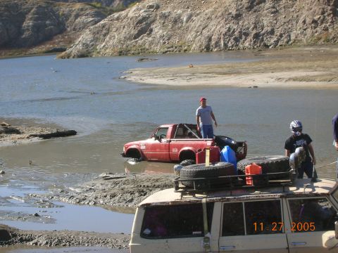 1985 Ford Bronco - Two off-road vehicles are partially submerged in water with people nearby.