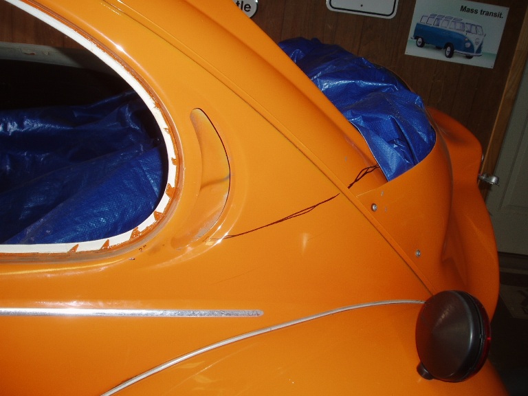 Orange-painted vintage car rear quarter panel with chrome trim and round taillight