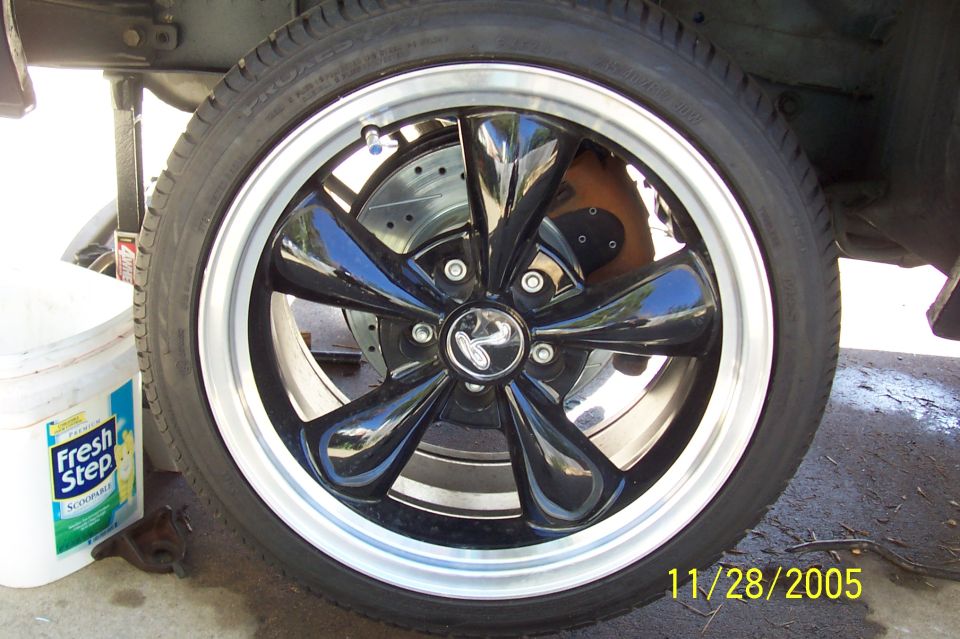 Black five-spoke wheel with polished lip and machined center cap, drilled rotor and red caliper behind