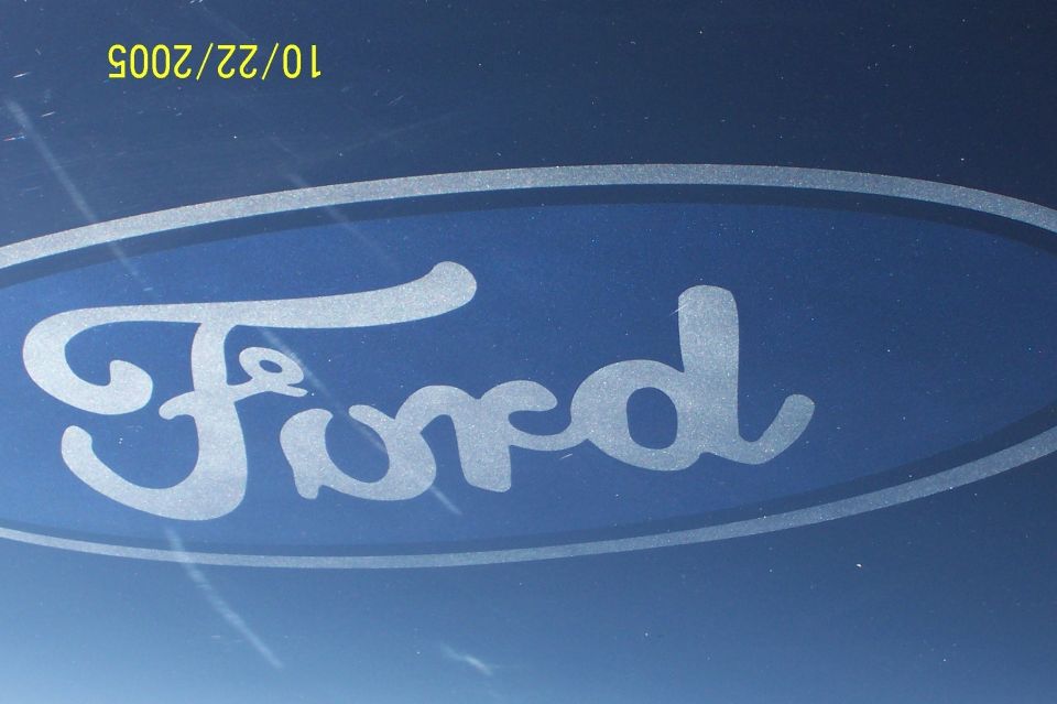 Silver Ford oval script decal on metallic blue paint, close-up