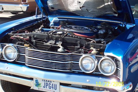 1969 Ford Ranchero - The engine bay of a blue 1969 Ford Ranchero is open, revealing its engine and chrome grille. A Texas license plate is visible on the front.