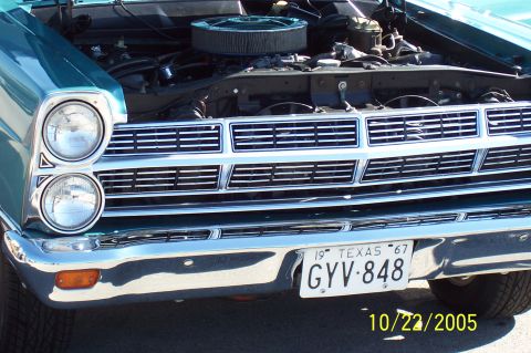 1969 Ford Ranchero - A teal Ford Ranchero with its hood open, revealing the engine and a prominent chrome grille, is viewed from the front.