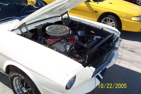 1969 Ford Ranchero - The engine bay of a white 1969 Ford Mustang is visible, with a yellow car parked behind it.