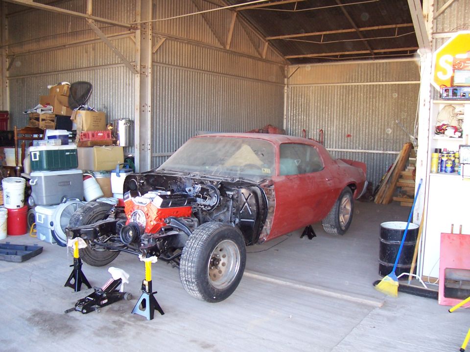Red 2nd-gen Camaro coupe with front end stripped, orange V8 exposed, on jack stands in shop