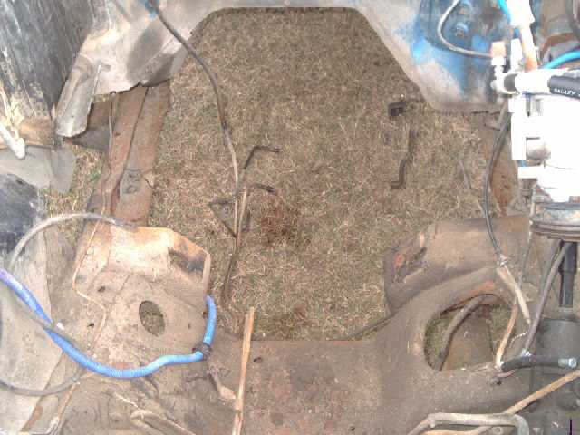 Bare metal cab floor pan covered in dirt and debris with wiring and brake lines exposed