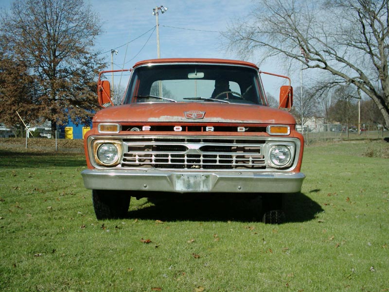 Front view of faded orange Ford pickup on grass, chrome grille and dual round headlights