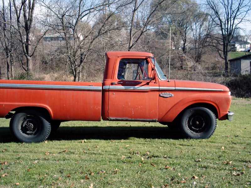 Driver-side profile of orange Ford long-bed pickup with chrome trim and black steel wheels