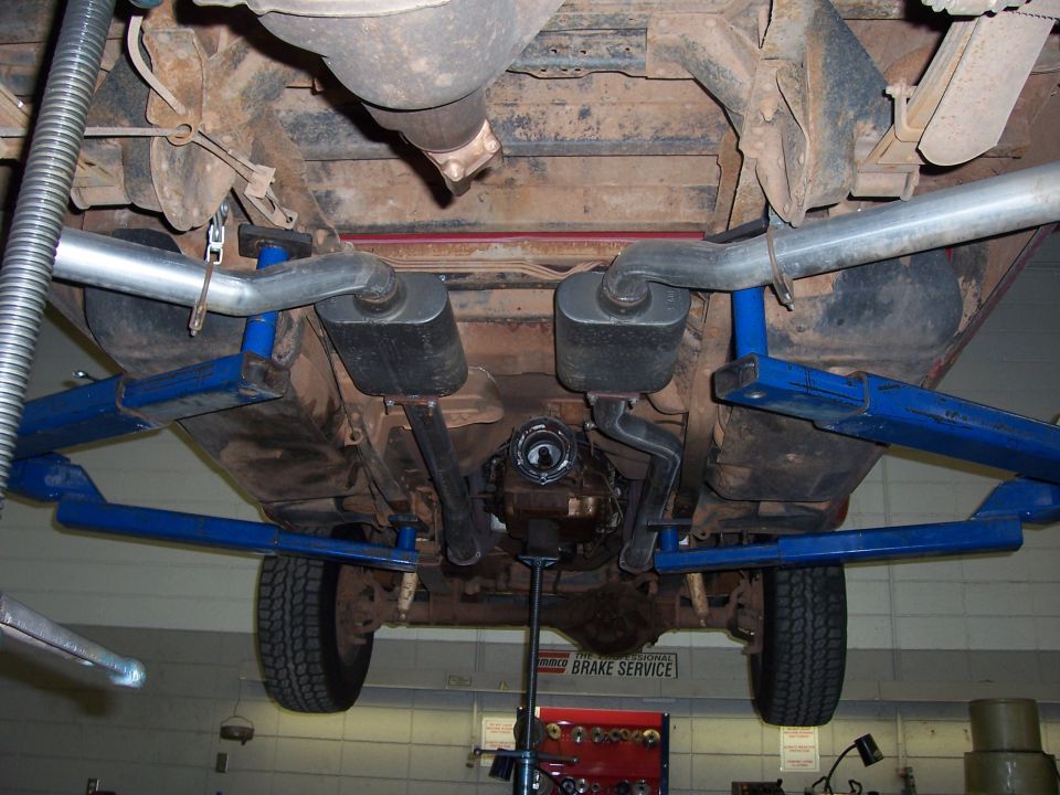 Underside of pickup on a shop lift showing exhaust, rear axle and blue lift arms