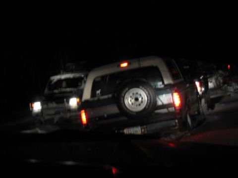 1992 Ford Bronco - A 1992 Ford Bronco and another SUV are stuck in the snow at night, with headlights and taillights illuminated.