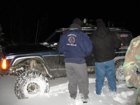 1992 Ford Bronco - A group of people stand around a Jeep Cherokee XJ that is stuck in the snow at night.