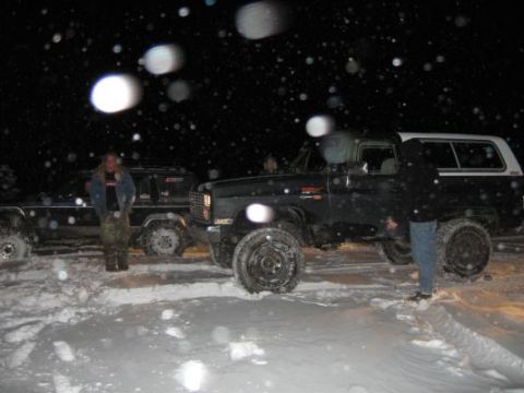 1992 Ford Bronco - Two SUVs are parked in the snow at night, with people standing around them.