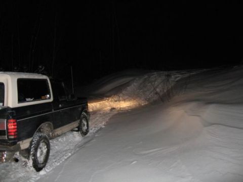 1992 Ford Bronco - A black 1992 Ford Bronco navigates a snow-covered road under the cover of darkness, its headlights cutting through the night.