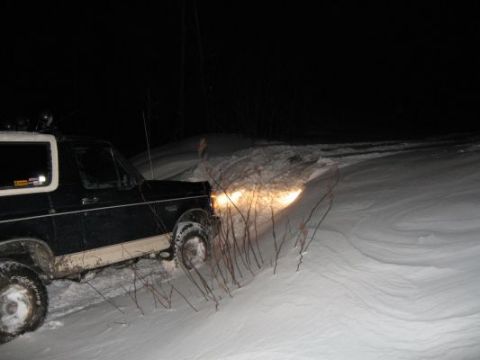 1992 Ford Bronco - Ford Bronco navigates a snow-covered path in the dark, headlights illuminating the way.