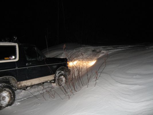 1992 Ford Bronco driving on a snowy road at night with headlights on