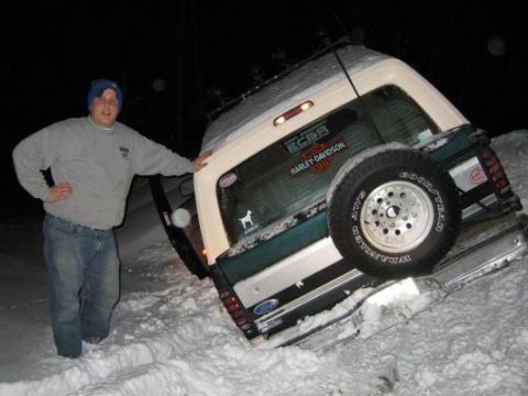 1992 Ford Bronco - A man stands beside a 1992 Ford Bronco that is stuck in the snow at night.