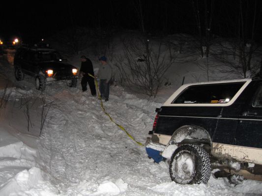 Two SUVs stuck in snow at night, one pulling the other with a yellow strap