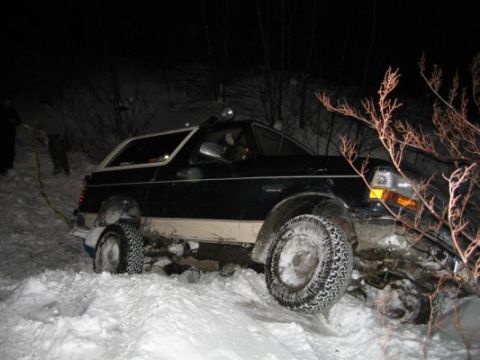 1992 Ford Bronco - A black Ford Bronco is stuck in deep snow at night, with trees and bushes visible in the background.