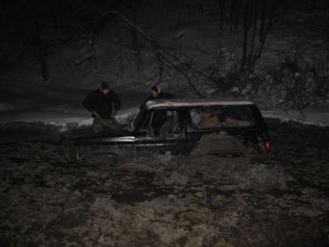 1992 Ford Bronco - A black SUV is stuck deep in mud with two people standing around it, seemingly in a difficult situation.
