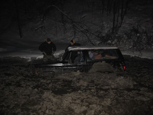 Black SUV stuck in mud with two people nearby