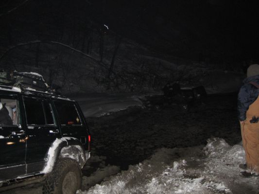 Several off-road vehicles are stuck in snow during nighttime conditions. One vehicle is in the foreground, and others are visible in the background
