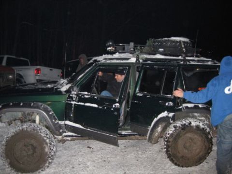 1992 Ford Bronco - Several people are gathered around a green Jeep Cherokee XJ in a snowy environment, with a white pickup truck visible behind it.