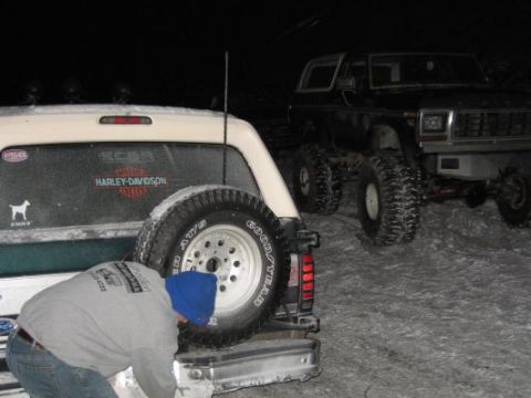 1992 Ford Bronco - Two vehicles are parked in a snowy landscape at night, with one person attending to the rear of the white SUV.