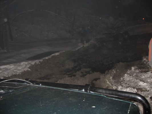 View from inside a vehicle driving through a snowy, possibly underground, area. A roll bar is visible in the foreground
