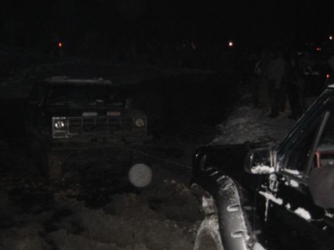 1992 Ford Bronco - Two trucks are stuck in the snow at night, with one being pulled by a tow strap.