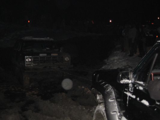 Two trucks stuck in snow at night, one being pulled by a tow strap