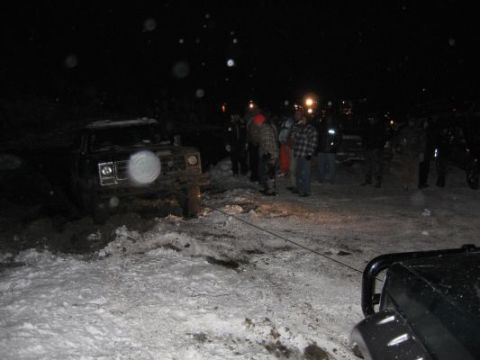1992 Ford Bronco - Several off-road vehicles appear stuck in a snowy, muddy area at night, with people gathered around.