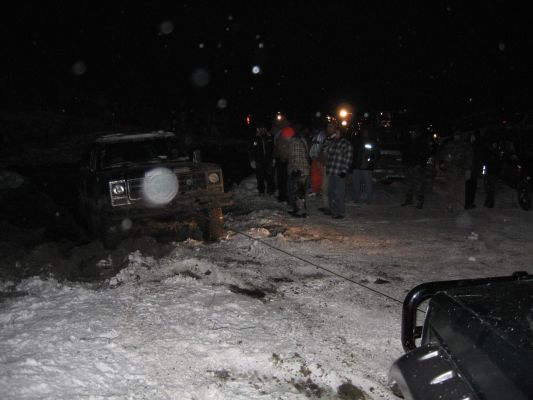 Truck stuck in snow, people around it, another vehicle in foreground