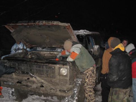 1992 Ford Bronco - A group of people inspect the engine of a heavily soiled 1980s Ford Bronco during a snowy outdoor event.
