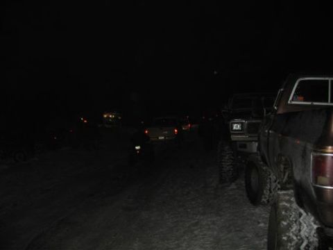 1992 Ford Bronco - A group of trucks are parked in a line at night, with some vehicles illuminated by their headlights.