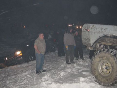 1992 Ford Bronco - A group of people stand around a light-colored Ford Bronco stuck in the snow at night.