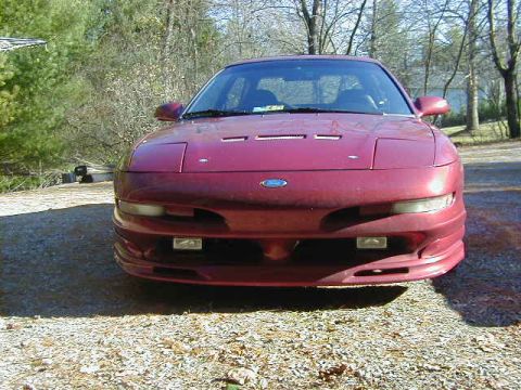 1994 Ford Probe - A red coupe sits parked outdoors on a gravel surface with trees in the background.