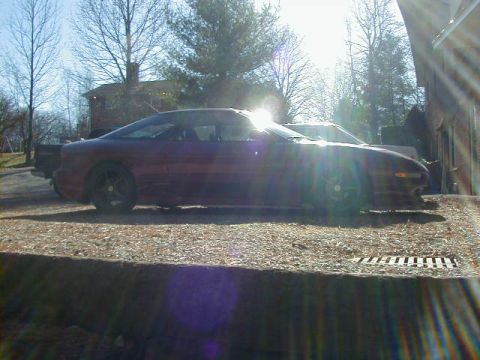 1994 Ford Probe - A red coupe sits parked on a gravel surface next to a building.