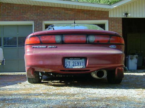 1994 Ford Probe - The rear of a red Ford Probe is parked in front of a brick garage. The license plate reads GT 2ENVY.