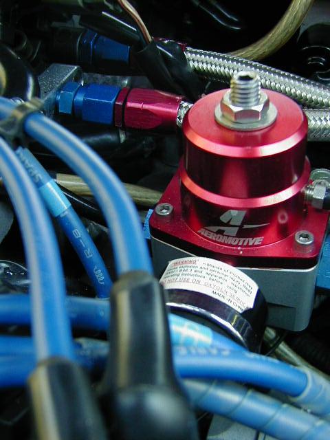 1994 Ford Probe - Close-up of a red Aeromotive fuel pressure regulator, part of a vehicle's fuel system, with visible warning text on a label.