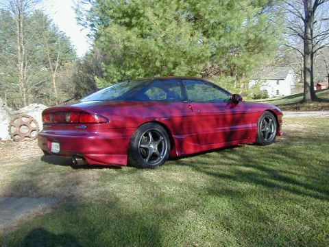 1994 Ford Probe - A red 1994 Ford Probe is parked on a grassy lawn in front of some trees and a house.