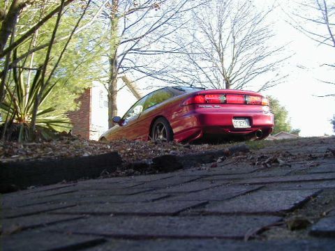 1994 Ford Probe - The rear of a red 1994 Ford Probe is visible, parked on an incline with foliage around it.