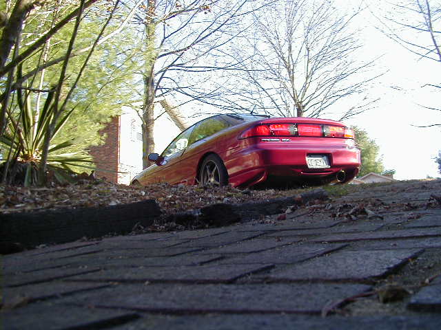 Red 1994 Ford Probe parked on a slope with trees and a brick building in the background